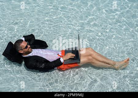 Erfolgreicher Geschäftsmann im Anzug im Poolwasser. Sommerurlaub und Reisekonzept. Lustiger Geschäftsmann im Anzug, schwimmt im Schwimmbad und hält die La Stockfoto