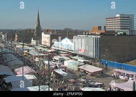 Besucher aus der Vogelperspektive in Romford auf einem großen Einzelhandelsmarkt im Freien in der städtischen Landschaft des Marktplatzes und darüber hinaus mit Marktständen und dem Turm der St. Edwards Kirche im Osten Londons Borough of Havering England UK Stockfoto