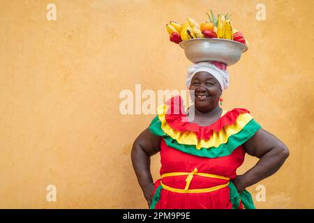 Fröhlicher, lächelnder Palenquera-Straßenverkäufer mit frischem Obst in der Altstadt von Cartagena, Kolumbien. Fröhliche afrokolumbianische Frau in traditionellen Kostümen. Stockfoto