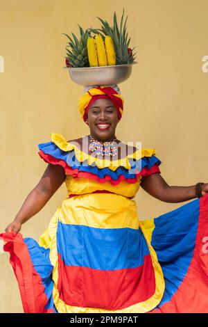 Fröhlich lächelnder Straßenverkäufer aus frischem Obst in Palenquera, der in Cartagena de Indias, Kolumbien, tanzt. Fröhliche afrokolumbianische Frau in traditionellen Kostümen. Stockfoto