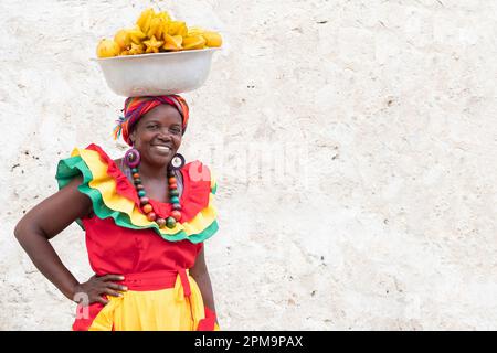 Fröhlicher, lächelnder Palenquera-Straßenverkäufer mit frischem Obst in der Altstadt von Cartagena, Kolumbien. Fröhliche afrokolumbianische Frau in traditionellen Kostümen. Stockfoto