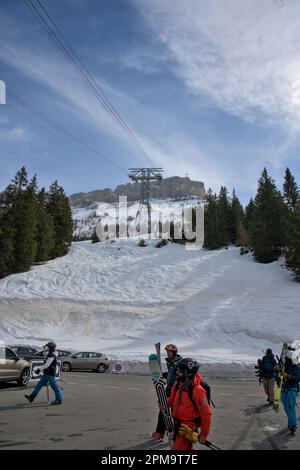 Eine Gruppe von Skifahrern, die die Straße und den Parkplatz überqueren, um die Seilbahn zu erreichen, die sie zum Gipfel zurückbringt Stockfoto