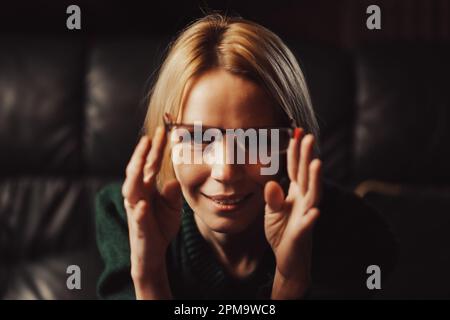 Eine Frau hält eine Brille in der Hand und schaut in die Kamera. Lehrer, Aufmerksamkeit, etwas lernen Konzept. Stockfoto
