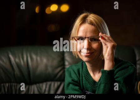 Eine Frau hält eine Brille in der Hand und schaut in die Kamera. Lehrer, Aufmerksamkeit, etwas lernen Konzept. Platz für Text Stockfoto