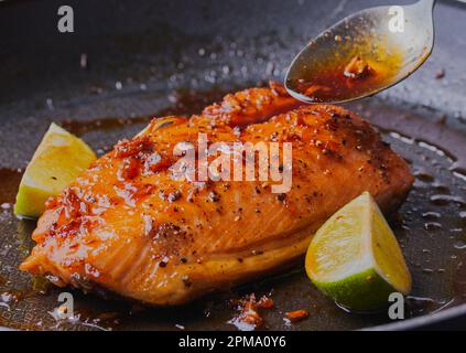 In der Pfanne gebratenes Lachsfilet mit Honig, Knoblauch, Gewürzen und Limettensaft, der in der Pfanne gebraten wird. Stockfoto