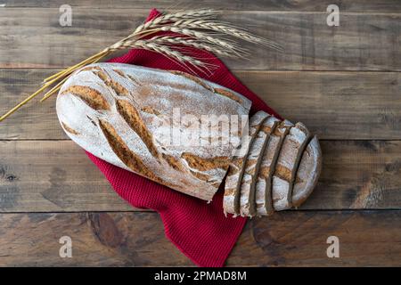 Ein Stück rustikales Brot auf Holzhintergrund mit Serviettendekorationen und Weizenohren. Speicherplatz kopieren. Draufsicht. Stockfoto