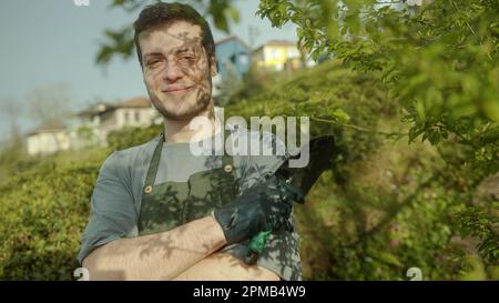 Porträt eines jungen, braunhaarigen, gut aussehenden männlichen Gärtners oder Bauern mit einer Schaufel in der Hand, die für die Kamera lächelt Stockfoto