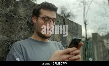 Mann mit Brille überrascht und lächelt, während er Smartphone Outdoors verwendet Stockfoto
