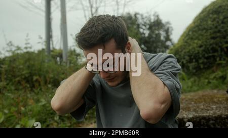 Junger Mann mit Brille kreist in Schmerzen, kämpft mit einem plötzlichen Auftreten von gesundheitlichen Problemen Stockfoto