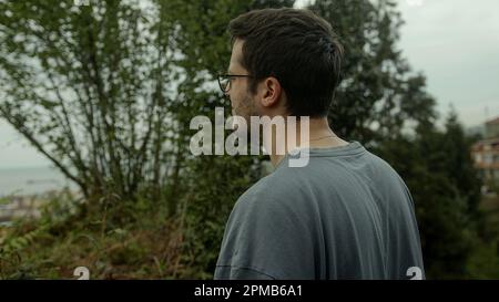 Junger brünetter Mann mit Brille auf einem Spaziergang im Wald - Rückansicht Stockfoto