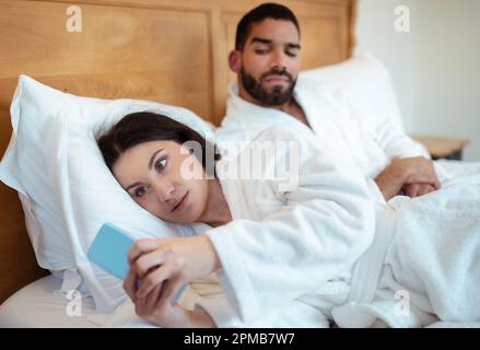Ehemann Sieht Betrügende Ehefrau, Die Im Schlafzimmer Sms Auf Dem Smartphone Schreibt Stockfoto