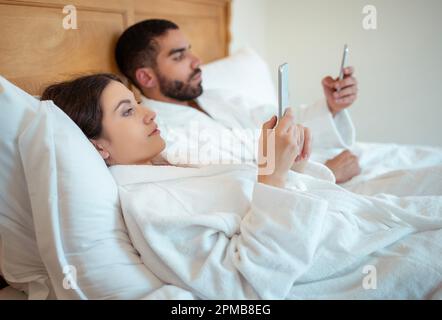 Paare, Die Telefone Benutzen, Texten Im Bett Liegen Und Bademäntel Im Haus Tragen Stockfoto
