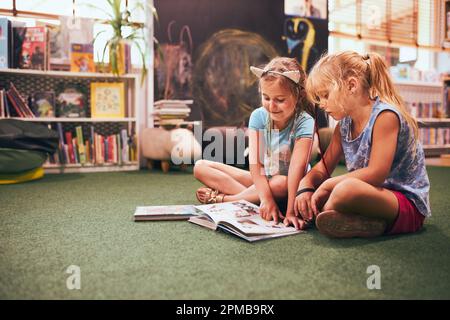 Zwei Grundschulmädchen machen Hausaufgaben in der Schulbibliothek. Schüler lernen aus Büchern. Schüler, die Spaß in der Bibliothek haben. Zurück in die Schule Stockfoto