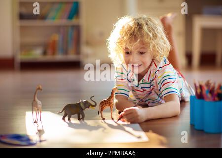 Ein Kinderschatten, der Tiere malt. Kinder spielen zu Hause. Lustiges Basteln für Kinder im Kindergarten. Ein kleiner Junge malt Giraffen und Elefanten im sonnigen Schlafzimmer. Stockfoto