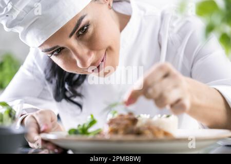 Eine junge Küchenchefin beendet das Essen mit Kräutern in der Restaurantküche - Nahaufnahme. Stockfoto