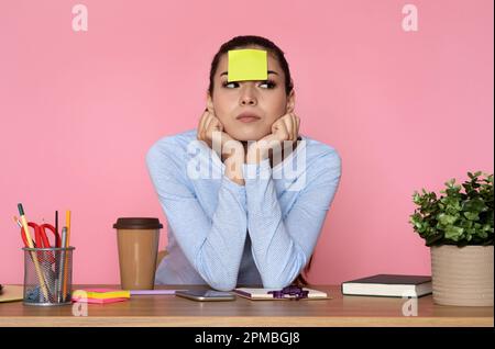 Müde junge Frau sitzt am Schreibtisch mit Aufklebern auf der Stirn Stockfoto