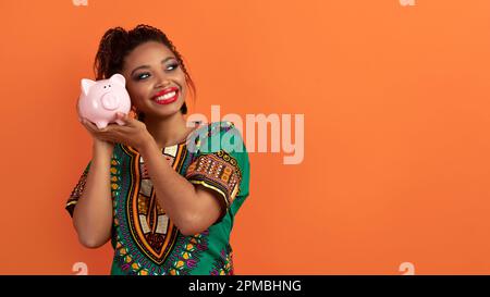 Fröhliche afrikanerin, die das Sparschwein neben dem Ohr hält Stockfoto