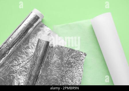 Backpapierrollen und Aluminiumfolie auf grünem Hintergrund Stockfoto