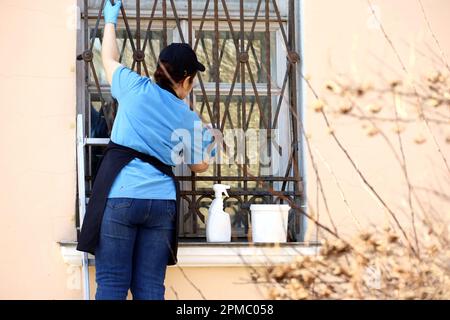 Fensterputz in der Stadt, Frau wäscht das Glas hinter Gittern an der alten Hausfassade Stockfoto