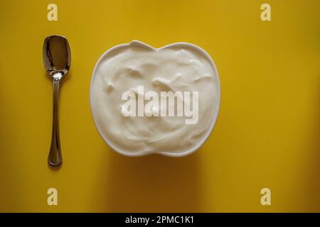 Eine Keramikschüssel Joghurt mit einem Löffel auf gelbem Hintergrund Stockfoto