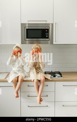 Ein Mädchen und ein Junge in Bademänteln sitzen in der Küche und schließen ihre Augen mit kandierten Orangen. Stockfoto