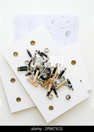 Möbelbeschläge. Ein Stapel verschiedener Montagezubehör auf einem weißen laminierten Spanplattenteil eines neuen Möbelstücks, Diagramm zur Selbstmontage von Möbeln Stockfoto