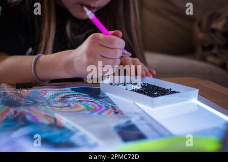 Ein kleines Mädchen, das Diamanten oder Perlen-Mosaik-Bilder macht. Bunte kleine Perlen kleben auf Leinwand. Fotoserie. Stockfoto