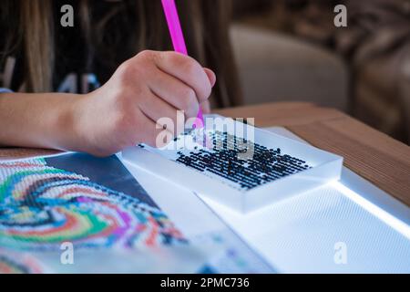 Ein kleines Mädchen, das Diamanten oder Perlen-Mosaik-Bilder macht. Bunte kleine Perlen kleben auf Leinwand. Fotoserie. Stockfoto