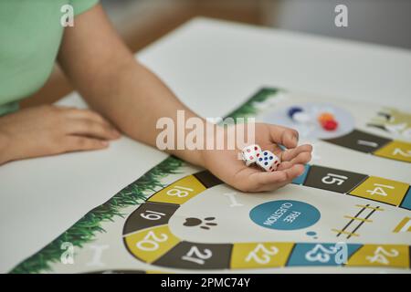 Großaufnahme einer nicht wiedererkennbaren jungen Frau, die bereit ist, Würfel zu werfen, während sie mit Freunden Brettspiele spielt, Kopierraum Stockfoto