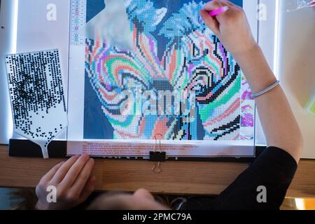 Ein kleines Mädchen, das Diamanten oder Perlen-Mosaik-Bilder macht. Bunte kleine Perlen kleben auf Leinwand. Fotoserie. Stockfoto