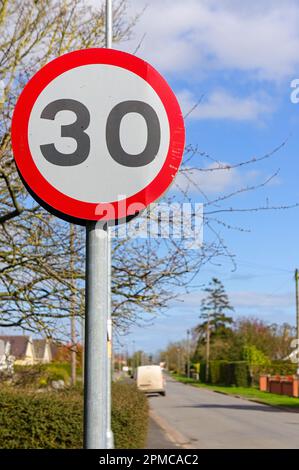 Ein britisches Geschwindigkeitsbegrenzungsschild mit einer Geschwindigkeit von 30 km/h und weicher Fokussierung auf die Vorstadtstraße im Hintergrund Stockfoto