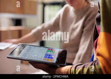 Lagerarbeiter analysieren Online-Kundenbestellungen auf digitalen Geräten und bereiten Pakete für den Versand vor. Vielfältige Mitarbeiter, die in der Warenlogistik im Lager arbeiten. Nahaufnahme Stockfoto