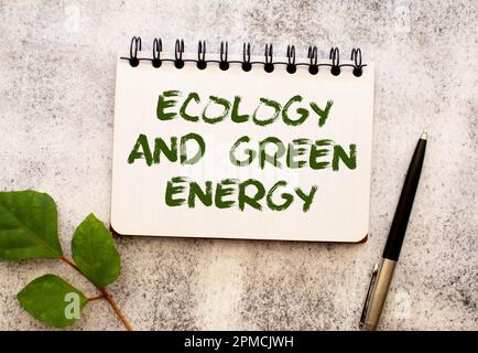 Zwischen zwei Blättern eines Notizbuchs auf einem grünen Streifen mit der Aufschrift „Ecology“ und „Green Energy“ befindet sich eine Lupe. Das Konzept ist "Ecolo" Stockfoto