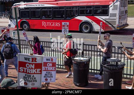 New Brunswick, New Jersey, USA. 12. April 2023. Ein Campus-Bus fährt an Rutgers Studenten und Dozenten vorbei, während sie an einem Streik auf dem Hauptcampus der Universität in New Brunswick teilnehmen. Die drei Fakultätsgewerkschaften, die etwa 9.000 Arbeiter an der Rutgers University, der staatlichen Universität von New Jersey, repräsentierten, streikten, nachdem sie in Verhandlungen mit der Regierung von Rutgers-Präsident Jonathan Holloway keinen Vertrag zustande gebracht hatten. Der Rundgang ist der erste in der 257-jährigen Geschichte der öffentlichen Universität und folgt fast einem Jahr der Verhandlungen um höhere Löhne und bessere Verträge. (Credi Stockfoto