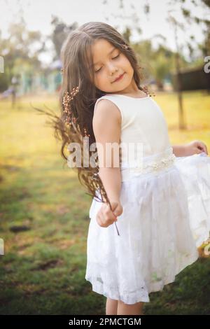 Kleines Mädchen in weißem Kleid, sie posiert für die Kamera mit einem wunderschönen Look, Kopierbereich, Kindertagsszene. Stockfoto