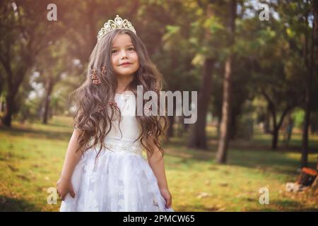 Kleines Mädchen in weißem Kleid und Prinzessinnen-Krone, sie posiert für die Kamera mit einem wunderschönen Look, Kopierbereich, Kindertagsmotiv. Stockfoto