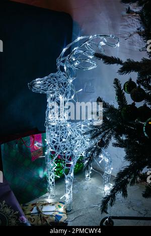 Neben den Christbaumzweigen befindet sich eine Statue mit Girlandeleuchten von Rentieren. Weihnachtsdekorationen. Stockfoto