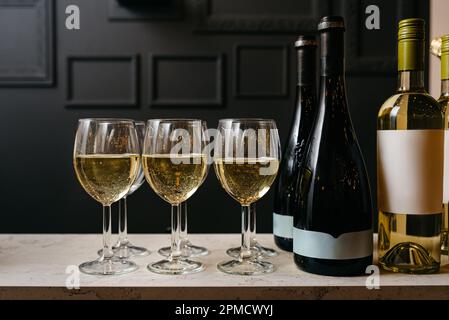 Weinflaschen und Gläser mit Weiß- und Rosenwein an der Bar. Luxuriöse Innenausstattung in einem modernen klassischen Loft (schwarz, goldfarben und weiß). Beige Marb Stockfoto
