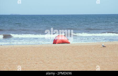 Am Sandstrand wurde ein orangefarbenes Zelt aufgestellt, dessen Wellen sich im Hintergrund von Virginia Beach, USA, bewegen. Stockfoto