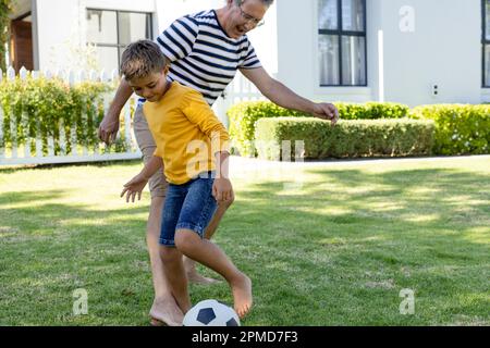 Fröhlicher weißer Großvater und Enkel, die Fußball spielen auf einem grasbedeckten Feld im Hof, Kopierraum Stockfoto