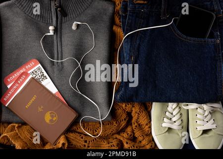 Nahaufnahme von grauem Pullover, Jeans, beigen Schuhen, Pass, Tickets, Smartphone und Kopfhörer Stockfoto