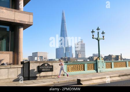 Junge Frau joggt über die Southwark Bridge über die Themse mit dem Shard Building im Hintergrund. London, England, Großbritannien. Stadt, Jogger, Bewegung, Joggen Stockfoto