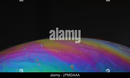 Makro eines irisierenden Seifenblasenfilms, der psychedelische Muster auf schwarzem Hintergrund bildet – abstrakte Farbtextur. Stockfoto