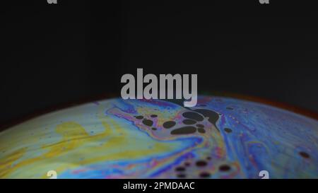 Makro eines irisierenden Seifenblasenfilms, der psychedelische Muster auf schwarzem Hintergrund bildet – abstrakte Farbtextur. Stockfoto