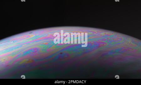Makro eines irisierenden Seifenblasenfilms, der psychedelische Muster auf schwarzem Hintergrund bildet – abstrakte Farbtextur. Stockfoto