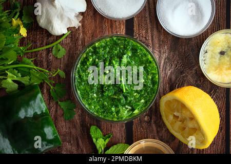 Cilantro-Mint Chutney in einer kleinen Glasschale, umgeben von Zutaten: Nahaufnahme eines traditionellen indischen Gewürzes, umgeben von frischen Zutaten Stockfoto