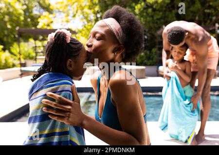 afroamerikanische Mutter küsst sich auf die Stirn ihrer Tochter und Vater wischte ihren Sohn am Pool im Resort Stockfoto