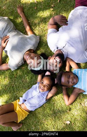 Blick von oben auf glückliche afroamerikanische Eltern und Kinder, die auf grasbewachsenem Land im Park liegen Stockfoto