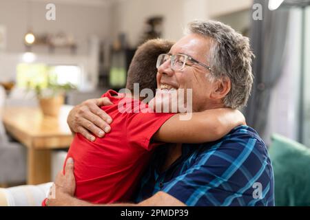 Lächelnder weißer Großvater umarmte den Enkel, während er im Wohnzimmer auf dem Sofa saß Stockfoto