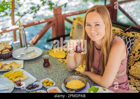 Eine Touristenfrau isst türkisches Frühstück. Türkischer Frühstückstisch. Gebäck, Gemüse, Gemüse, Gemüse, Oliven, Käse, Spiegeleier, Gewürze, Marmelade, Honig, Tee Stockfoto